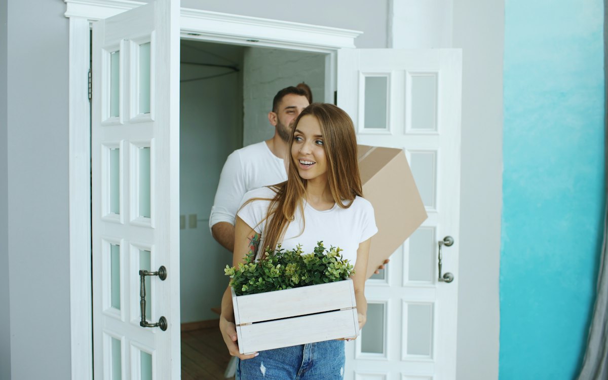 A couple carrying boxes and a plant into a new home